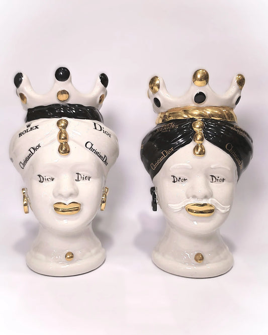 Coppia di Teste di Moro in ceramica bianca lucida con turbanti neri e bianchi decorati da loghi fashion neri e dorati, completate da corone regali e labbra con finitura in oro zecchino. Queste sculture ornamentali di design pop art fondono la tradizione ceramica siciliana con l'estetica del lusso moderno, rappresentando un complemento d'arredo audace ed esclusivo per interni ricercati.