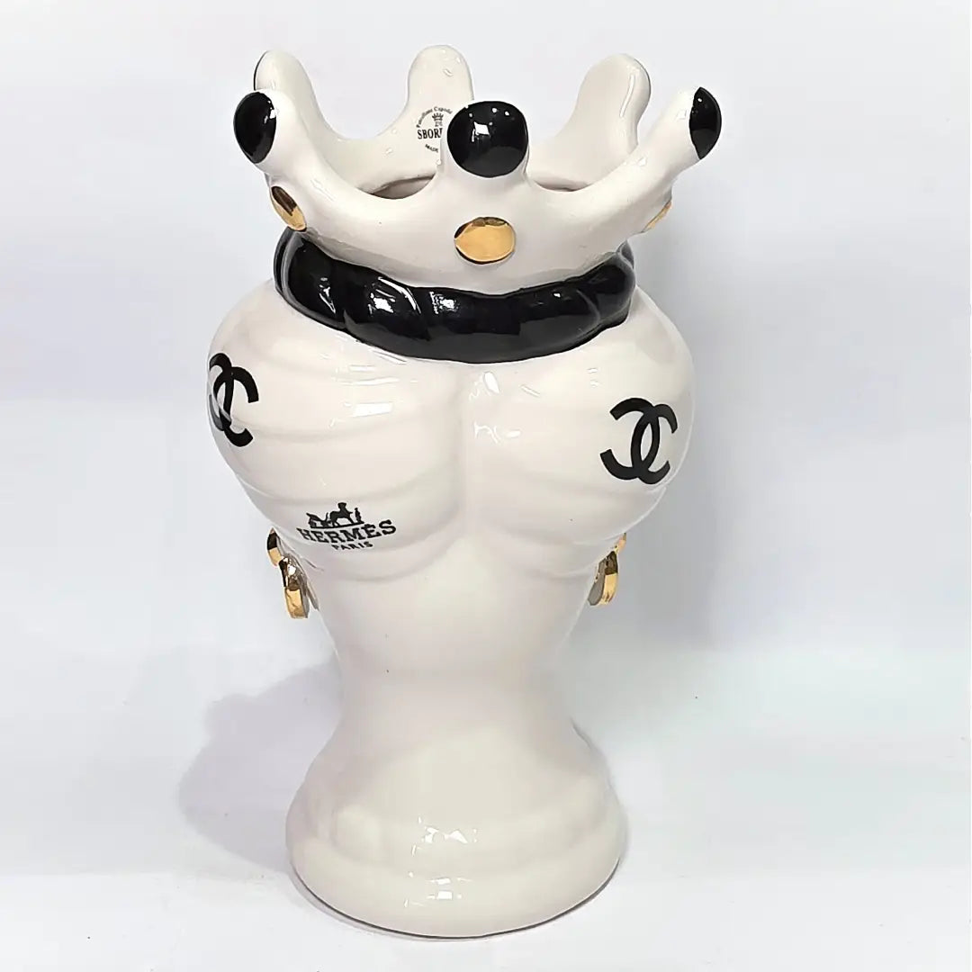Coppia di Teste di Moro in ceramica bianca lucida con turbanti neri e bianchi decorati da loghi fashion neri e dorati, completate da corone regali e labbra con finitura in oro zecchino. Queste sculture ornamentali di design pop art fondono la tradizione ceramica siciliana con l'estetica del lusso moderno, rappresentando un complemento d'arredo audace ed esclusivo per interni ricercati.