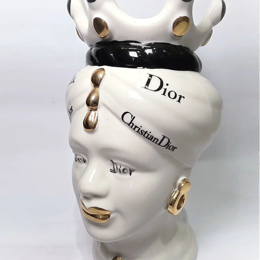 Coppia di Teste di Moro in ceramica bianca lucida con turbanti neri e bianchi decorati da loghi fashion neri e dorati, completate da corone regali e labbra con finitura in oro zecchino. Queste sculture ornamentali di design pop art fondono la tradizione ceramica siciliana con l'estetica del lusso moderno, rappresentando un complemento d'arredo audace ed esclusivo per interni ricercati.