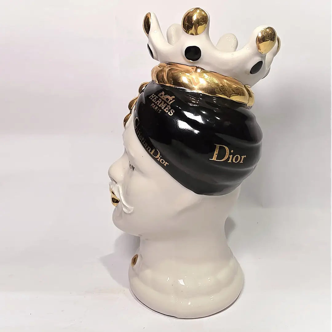 Coppia di Teste di Moro in ceramica bianca lucida con turbanti neri e bianchi decorati da loghi fashion neri e dorati, completate da corone regali e labbra con finitura in oro zecchino. Queste sculture ornamentali di design pop art fondono la tradizione ceramica siciliana con l'estetica del lusso moderno, rappresentando un complemento d'arredo audace ed esclusivo per interni ricercati.