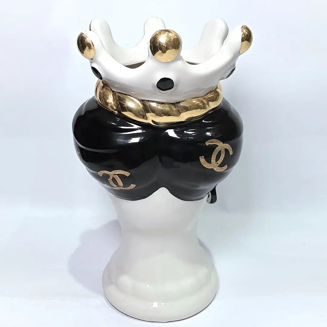 Coppia di Teste di Moro in ceramica bianca lucida con turbanti neri e bianchi decorati da loghi fashion neri e dorati, completate da corone regali e labbra con finitura in oro zecchino. Queste sculture ornamentali di design pop art fondono la tradizione ceramica siciliana con l'estetica del lusso moderno, rappresentando un complemento d'arredo audace ed esclusivo per interni ricercati.