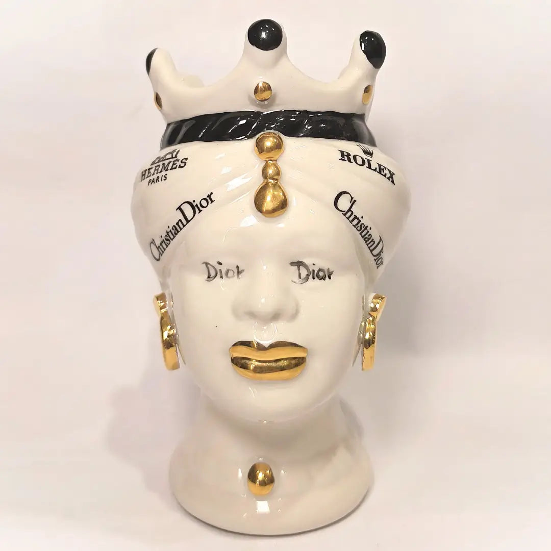Coppia di Teste di Moro in ceramica bianca lucida con turbanti neri e bianchi decorati da loghi fashion neri e dorati, completate da corone regali e labbra con finitura in oro zecchino. Queste sculture ornamentali di design pop art fondono la tradizione ceramica siciliana con l'estetica del lusso moderno, rappresentando un complemento d'arredo audace ed esclusivo per interni ricercati.