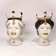Coppia di Teste di Moro in ceramica bianca lucida con turbanti neri e bianchi decorati da loghi fashion neri e dorati, completate da corone regali e labbra con finitura in oro zecchino. Queste sculture ornamentali di design pop art fondono la tradizione ceramica siciliana con l'estetica del lusso moderno, rappresentando un complemento d'arredo audace ed esclusivo per interni ricercati.