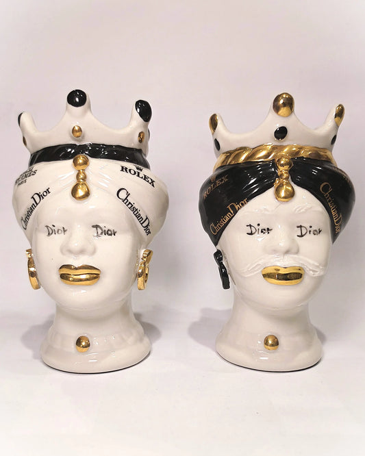 Coppia di Teste di Moro in ceramica bianca lucida con turbanti neri e bianchi decorati da loghi fashion neri e dorati, completate da corone regali e labbra con finitura in oro zecchino. Queste sculture ornamentali di design pop art fondono la tradizione ceramica siciliana con l'estetica del lusso moderno, rappresentando un complemento d'arredo audace ed esclusivo per interni ricercati.