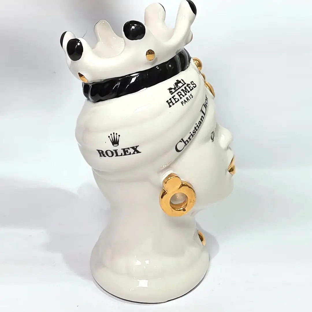 Coppia di Teste di Moro in ceramica bianca lucida con turbanti neri e bianchi decorati da loghi fashion neri e dorati, completate da corone regali e labbra con finitura in oro zecchino. Queste sculture ornamentali di design pop art fondono la tradizione ceramica siciliana con l'estetica del lusso moderno, rappresentando un complemento d'arredo audace ed esclusivo per interni ricercati.