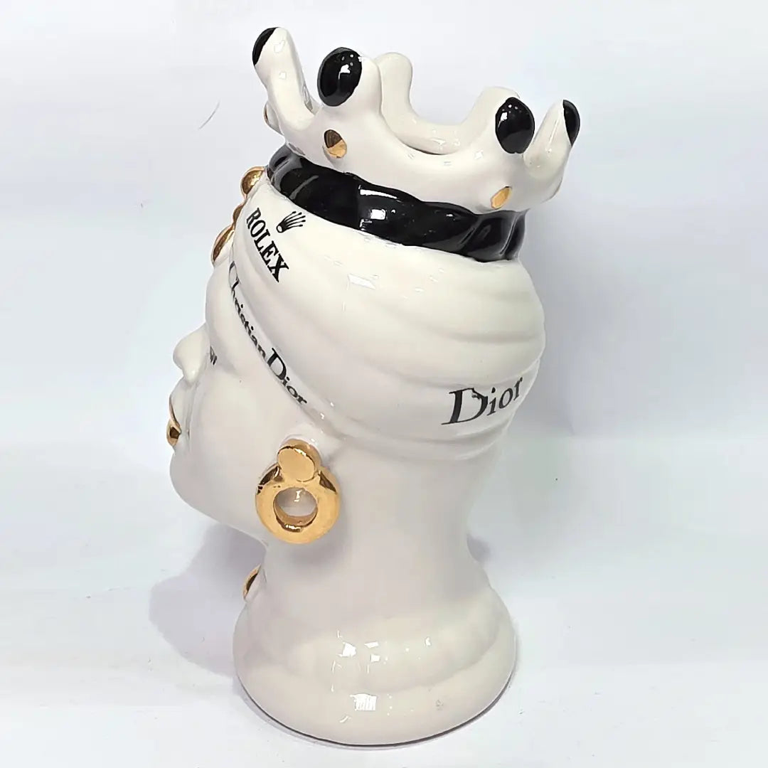 Coppia di Teste di Moro in ceramica bianca lucida con turbanti neri e bianchi decorati da loghi fashion neri e dorati, completate da corone regali e labbra con finitura in oro zecchino. Queste sculture ornamentali di design pop art fondono la tradizione ceramica siciliana con l'estetica del lusso moderno, rappresentando un complemento d'arredo audace ed esclusivo per interni ricercati.