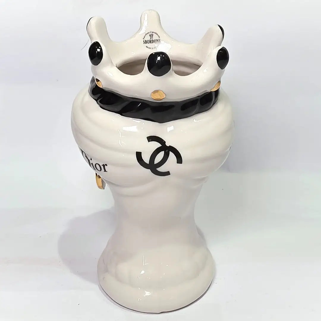 Coppia di Teste di Moro in ceramica bianca lucida con turbanti neri e bianchi decorati da loghi fashion neri e dorati, completate da corone regali e labbra con finitura in oro zecchino. Queste sculture ornamentali di design pop art fondono la tradizione ceramica siciliana con l'estetica del lusso moderno, rappresentando un complemento d'arredo audace ed esclusivo per interni ricercati.
