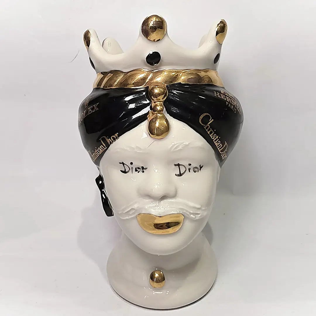 Coppia di Teste di Moro in ceramica bianca lucida con turbanti neri e bianchi decorati da loghi fashion neri e dorati, completate da corone regali e labbra con finitura in oro zecchino. Queste sculture ornamentali di design pop art fondono la tradizione ceramica siciliana con l'estetica del lusso moderno, rappresentando un complemento d'arredo audace ed esclusivo per interni ricercati.
