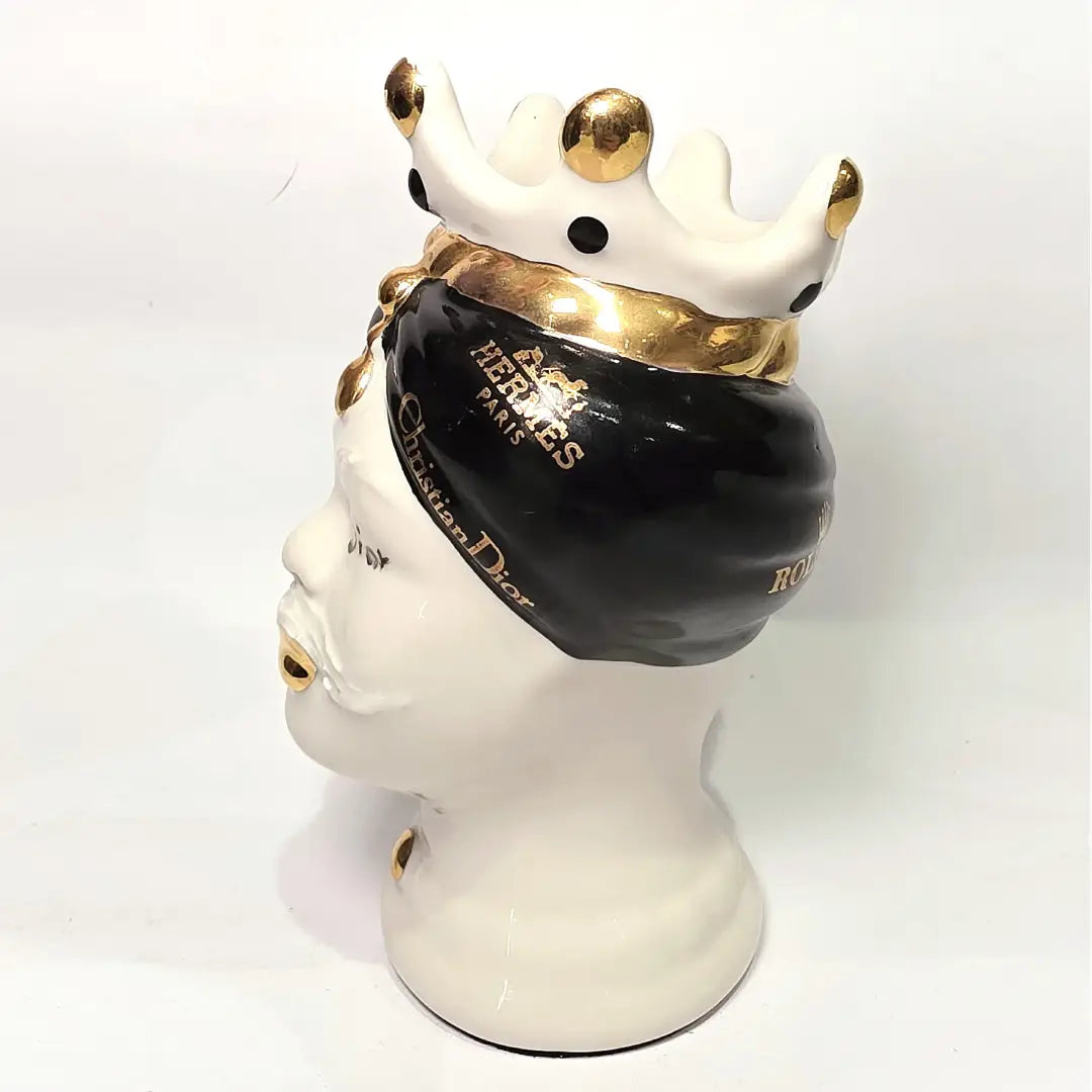 Coppia di Teste di Moro in ceramica bianca lucida con turbanti neri e bianchi decorati da loghi fashion neri e dorati, completate da corone regali e labbra con finitura in oro zecchino. Queste sculture ornamentali di design pop art fondono la tradizione ceramica siciliana con l'estetica del lusso moderno, rappresentando un complemento d'arredo audace ed esclusivo per interni ricercati.