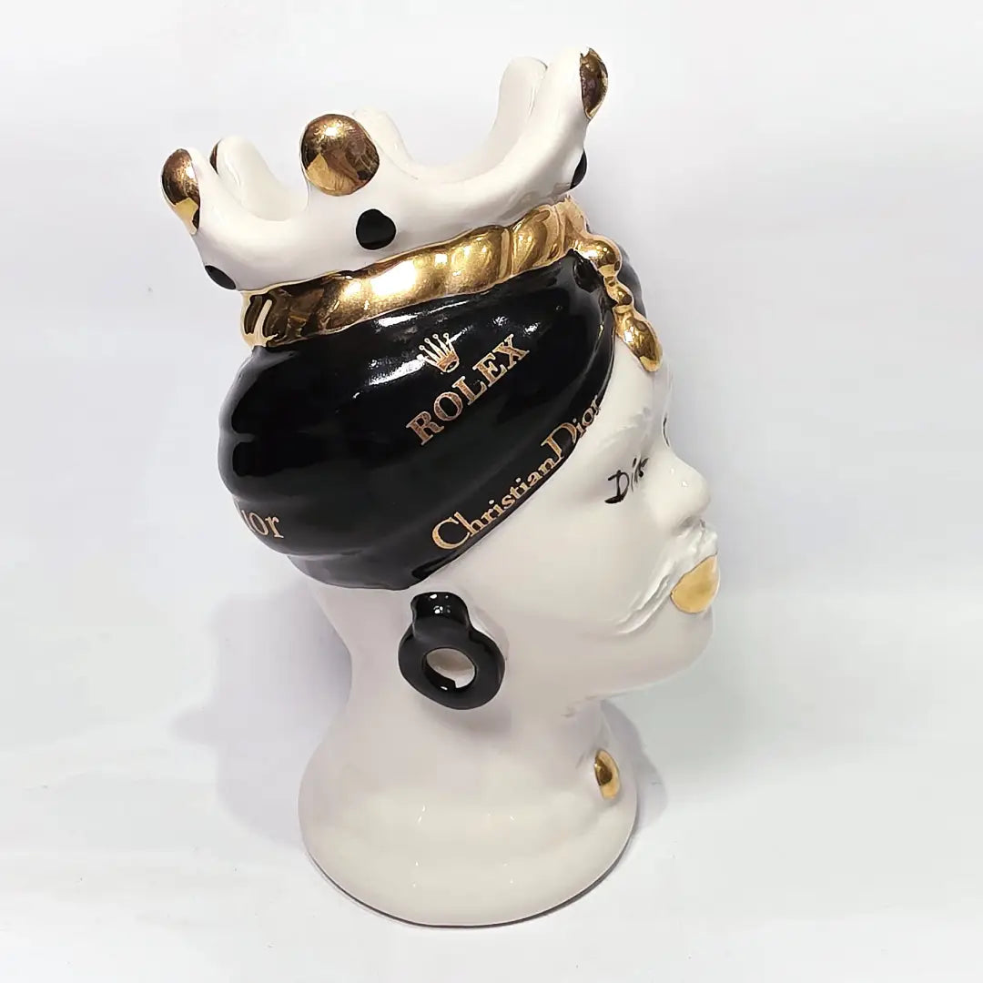 Coppia di Teste di Moro in ceramica bianca lucida con turbanti neri e bianchi decorati da loghi fashion neri e dorati, completate da corone regali e labbra con finitura in oro zecchino. Queste sculture ornamentali di design pop art fondono la tradizione ceramica siciliana con l'estetica del lusso moderno, rappresentando un complemento d'arredo audace ed esclusivo per interni ricercati.