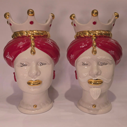 Coppia di Teste di Moro in ceramica bianca lucida con turbanti rosso ciliegia decorati da loghi fashion bianchi, completate da corone regali e labbra con finitura in oro zecchino. Queste sculture ornamentali di design pop art fondono la tradizione ceramica siciliana con l'estetica del lusso moderno, rappresentando un complemento d'arredo audace ed esclusivo per interni ricercati.