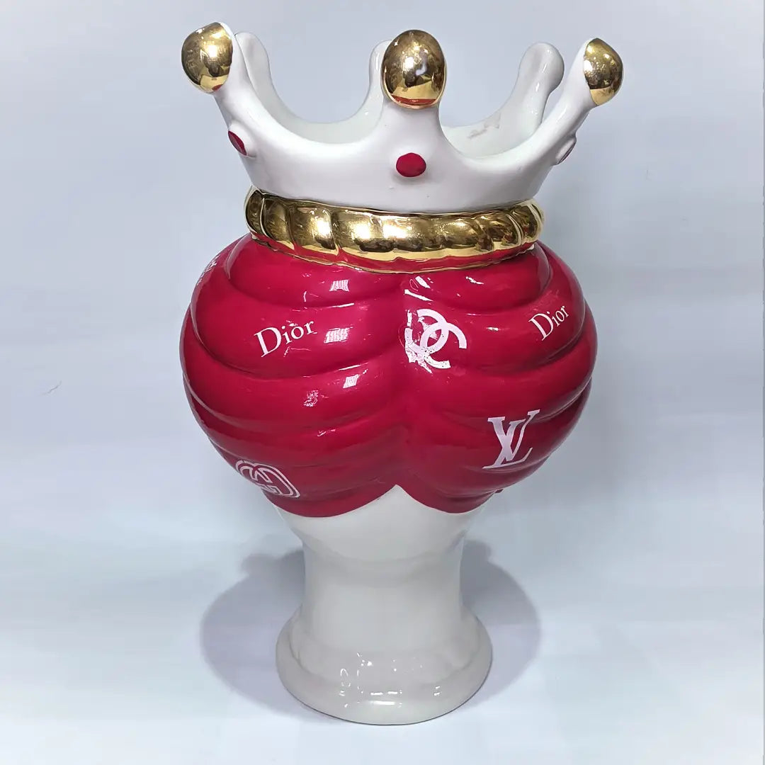 Coppia di Teste di Moro in ceramica bianca lucida con turbanti rosso ciliegia decorati da loghi fashion bianchi, completate da corone regali e labbra con finitura in oro zecchino. Queste sculture ornamentali di design pop art fondono la tradizione ceramica siciliana con l'estetica del lusso moderno, rappresentando un complemento d'arredo audace ed esclusivo per interni ricercati.
