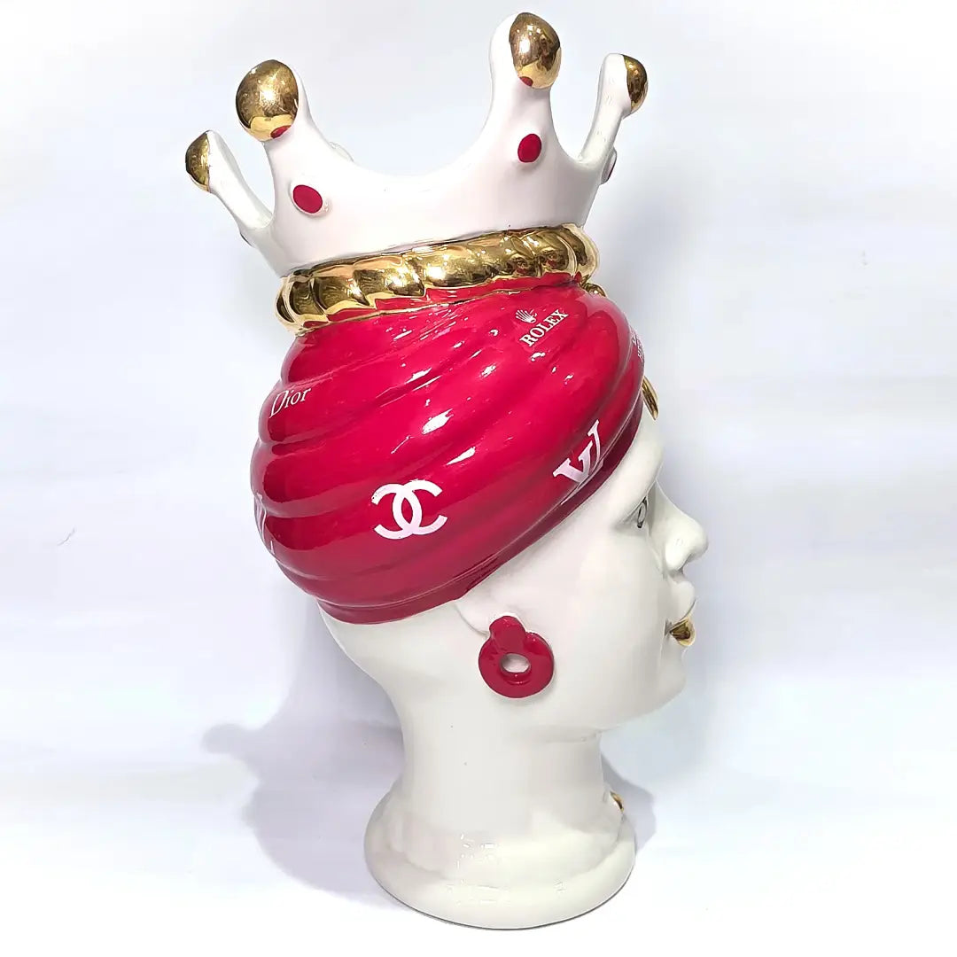 Coppia di Teste di Moro in ceramica bianca lucida con turbanti rosso ciliegia decorati da loghi fashion bianchi, completate da corone regali e labbra con finitura in oro zecchino. Queste sculture ornamentali di design pop art fondono la tradizione ceramica siciliana con l'estetica del lusso moderno, rappresentando un complemento d'arredo audace ed esclusivo per interni ricercati.