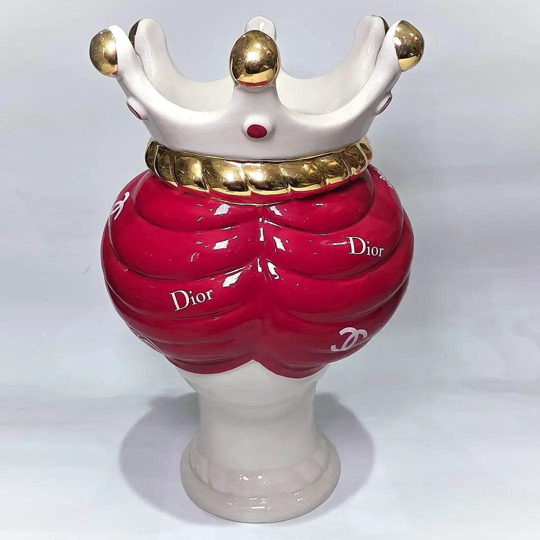 Coppia di Teste di Moro in ceramica bianca lucida con turbanti rosso ciliegia decorati da loghi fashion bianchi, completate da corone regali e labbra con finitura in oro zecchino. Queste sculture ornamentali di design pop art fondono la tradizione ceramica siciliana con l'estetica del lusso moderno, rappresentando un complemento d'arredo audace ed esclusivo per interni ricercati.