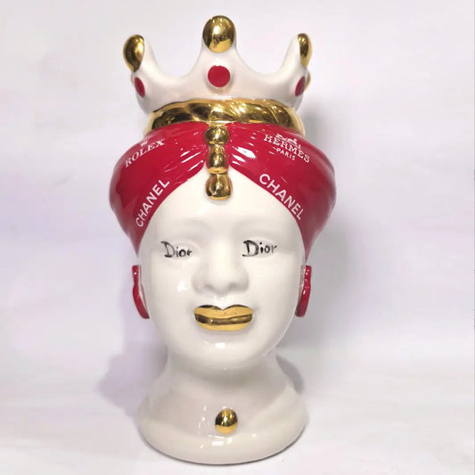 Coppia di Teste di Moro in ceramica bianca lucida con turbanti rosso ciliegia decorati da loghi fashion bianchi, completate da corone regali e labbra con finitura in oro zecchino. Queste sculture ornamentali di design pop art fondono la tradizione ceramica siciliana con l'estetica del lusso moderno, rappresentando un complemento d'arredo audace ed esclusivo per interni ricercati.