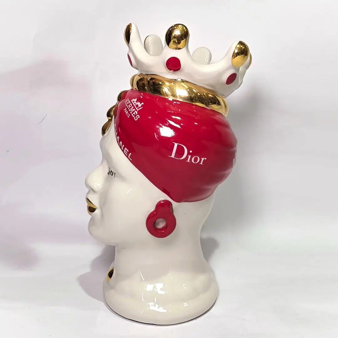 Coppia di Teste di Moro in ceramica bianca lucida con turbanti rosso ciliegia decorati da loghi fashion bianchi, completate da corone regali e labbra con finitura in oro zecchino. Queste sculture ornamentali di design pop art fondono la tradizione ceramica siciliana con l'estetica del lusso moderno, rappresentando un complemento d'arredo audace ed esclusivo per interni ricercati.
