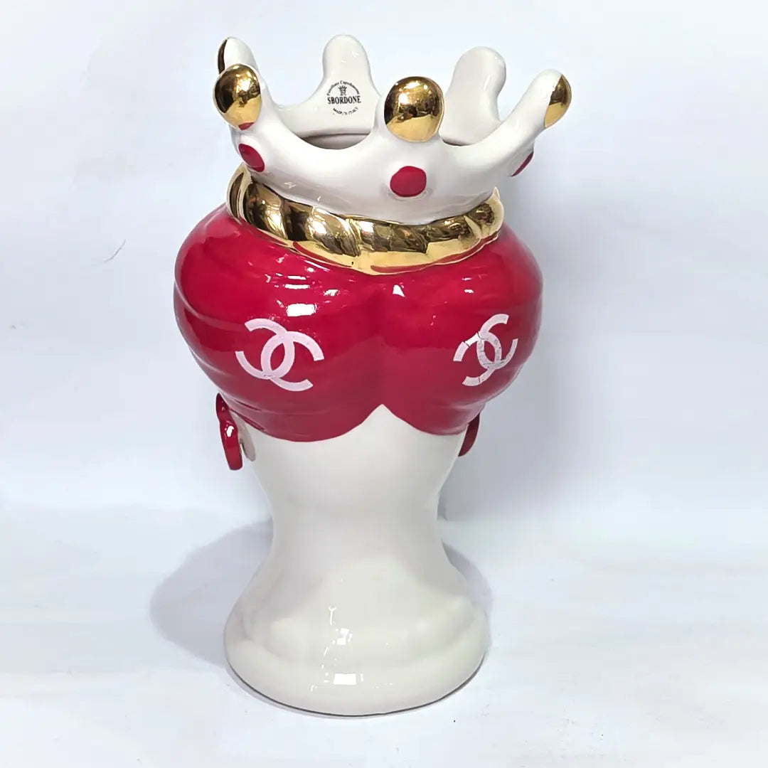 Coppia di Teste di Moro in ceramica bianca lucida con turbanti rosso ciliegia decorati da loghi fashion bianchi, completate da corone regali e labbra con finitura in oro zecchino. Queste sculture ornamentali di design pop art fondono la tradizione ceramica siciliana con l'estetica del lusso moderno, rappresentando un complemento d'arredo audace ed esclusivo per interni ricercati.