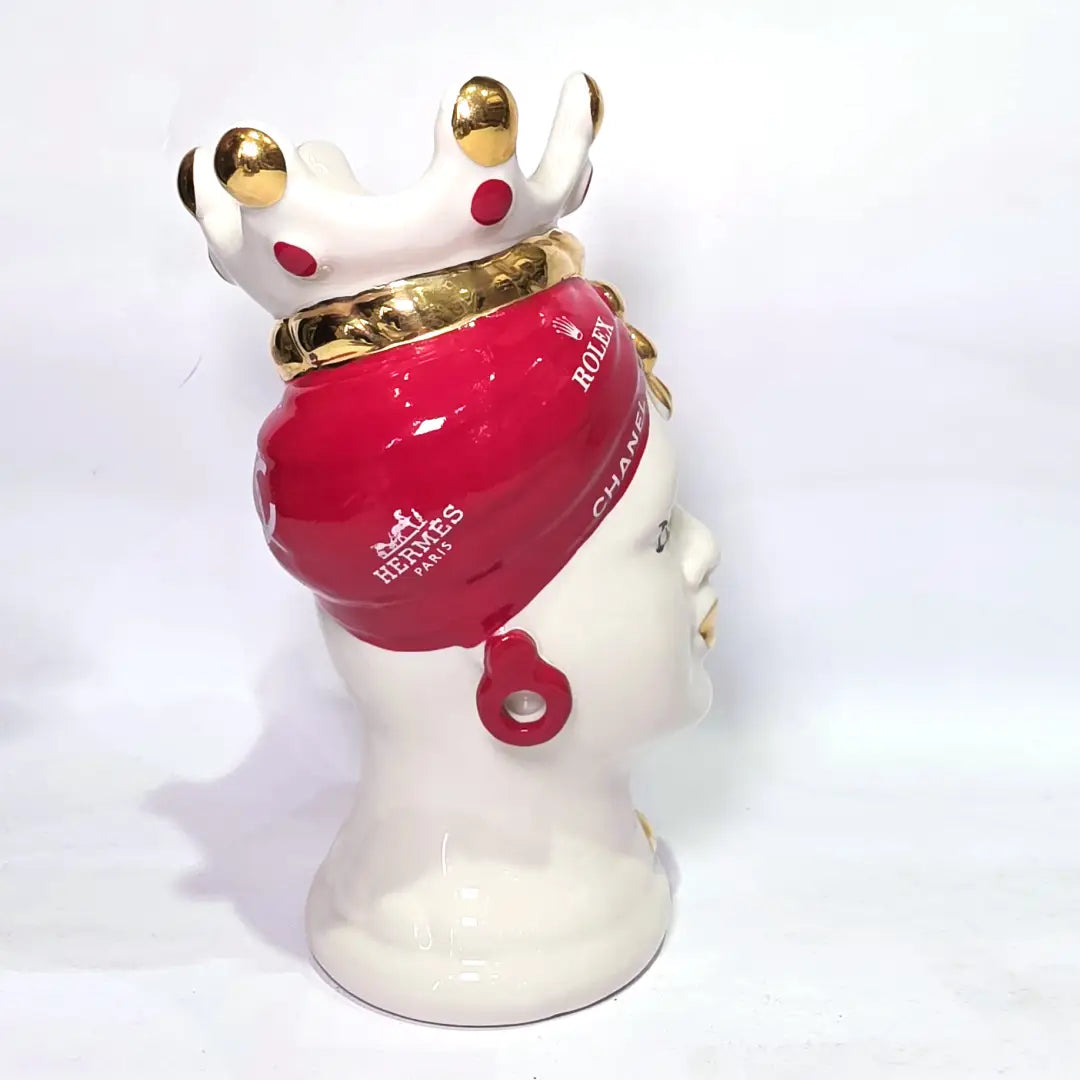 Coppia di Teste di Moro in ceramica bianca lucida con turbanti rosso ciliegia decorati da loghi fashion bianchi, completate da corone regali e labbra con finitura in oro zecchino. Queste sculture ornamentali di design pop art fondono la tradizione ceramica siciliana con l'estetica del lusso moderno, rappresentando un complemento d'arredo audace ed esclusivo per interni ricercati.