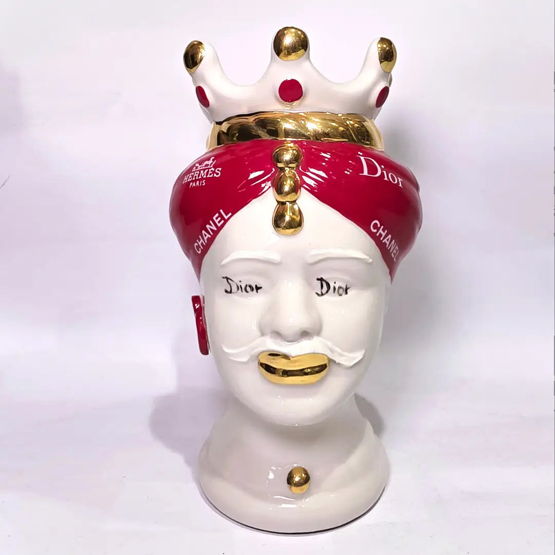 Coppia di Teste di Moro in ceramica bianca lucida con turbanti rosso ciliegia decorati da loghi fashion bianchi, completate da corone regali e labbra con finitura in oro zecchino. Queste sculture ornamentali di design pop art fondono la tradizione ceramica siciliana con l'estetica del lusso moderno, rappresentando un complemento d'arredo audace ed esclusivo per interni ricercati.