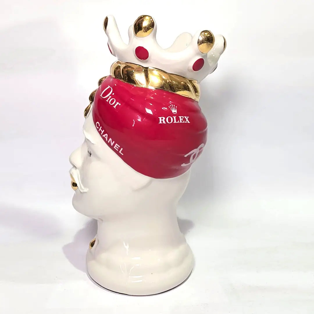 Coppia di Teste di Moro in ceramica bianca lucida con turbanti rosso ciliegia decorati da loghi fashion bianchi, completate da corone regali e labbra con finitura in oro zecchino. Queste sculture ornamentali di design pop art fondono la tradizione ceramica siciliana con l'estetica del lusso moderno, rappresentando un complemento d'arredo audace ed esclusivo per interni ricercati.