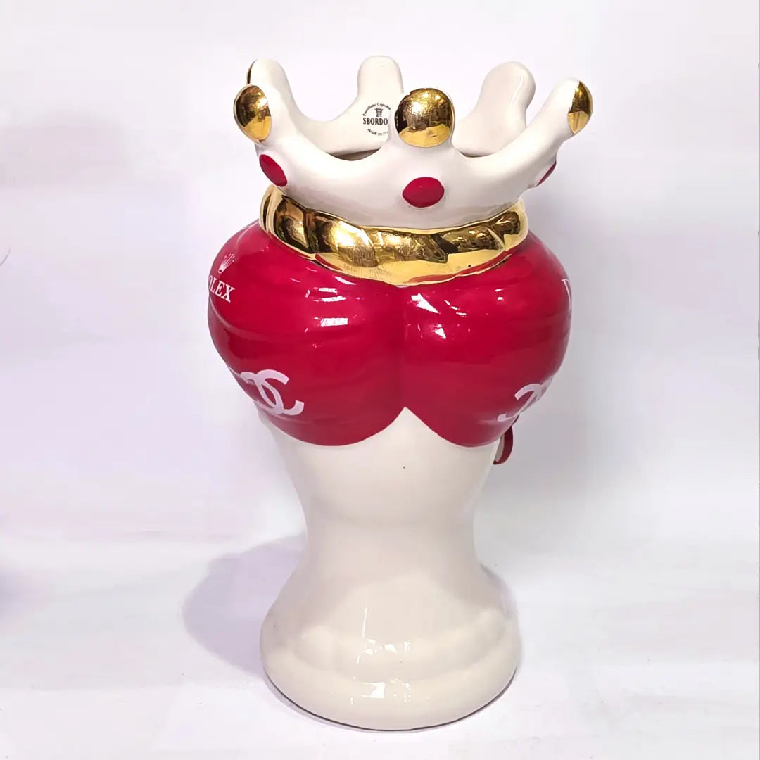 Coppia di Teste di Moro in ceramica bianca lucida con turbanti rosso ciliegia decorati da loghi fashion bianchi, completate da corone regali e labbra con finitura in oro zecchino. Queste sculture ornamentali di design pop art fondono la tradizione ceramica siciliana con l'estetica del lusso moderno, rappresentando un complemento d'arredo audace ed esclusivo per interni ricercati.