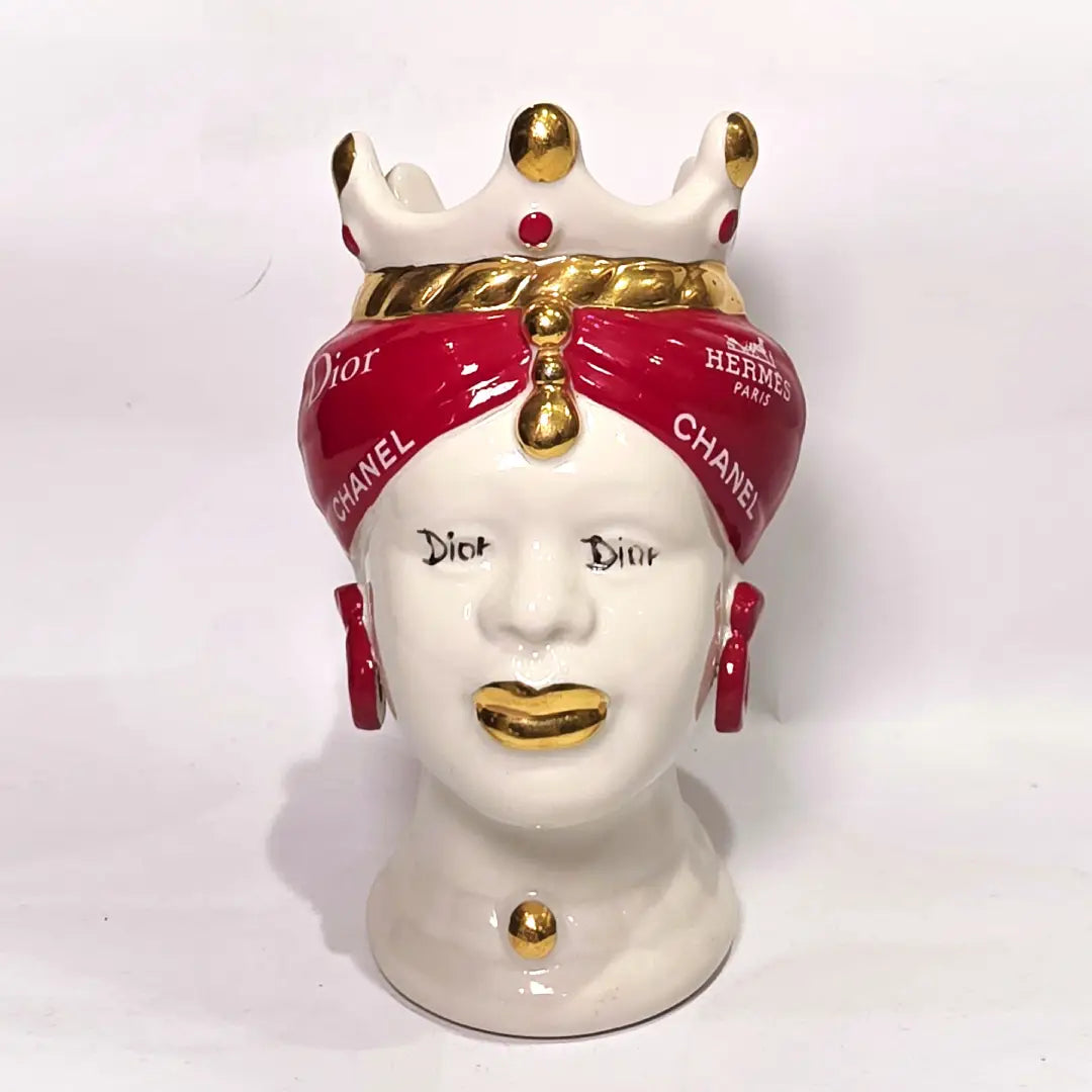 Coppia di Teste di Moro in ceramica bianca lucida con turbanti rosso ciliegia decorati da loghi fashion bianchi, completate da corone regali e labbra con finitura in oro zecchino. Queste sculture ornamentali di design pop art fondono la tradizione ceramica siciliana con l'estetica del lusso moderno, rappresentando un complemento d'arredo audace ed esclusivo per interni ricercati.