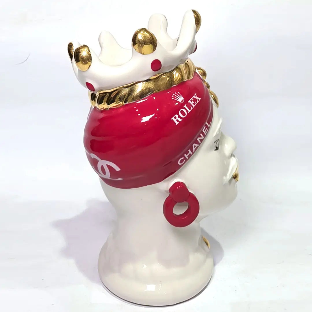 Coppia di Teste di Moro in ceramica bianca lucida con turbanti rosso ciliegia decorati da loghi fashion bianchi, completate da corone regali e labbra con finitura in oro zecchino. Queste sculture ornamentali di design pop art fondono la tradizione ceramica siciliana con l'estetica del lusso moderno, rappresentando un complemento d'arredo audace ed esclusivo per interni ricercati.