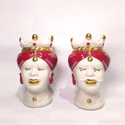 Coppia di Teste di Moro in ceramica bianca lucida con turbanti rosso ciliegia decorati da loghi fashion bianchi, completate da corone regali e labbra con finitura in oro zecchino. Queste sculture ornamentali di design pop art fondono la tradizione ceramica siciliana con l'estetica del lusso moderno, rappresentando un complemento d'arredo audace ed esclusivo per interni ricercati.