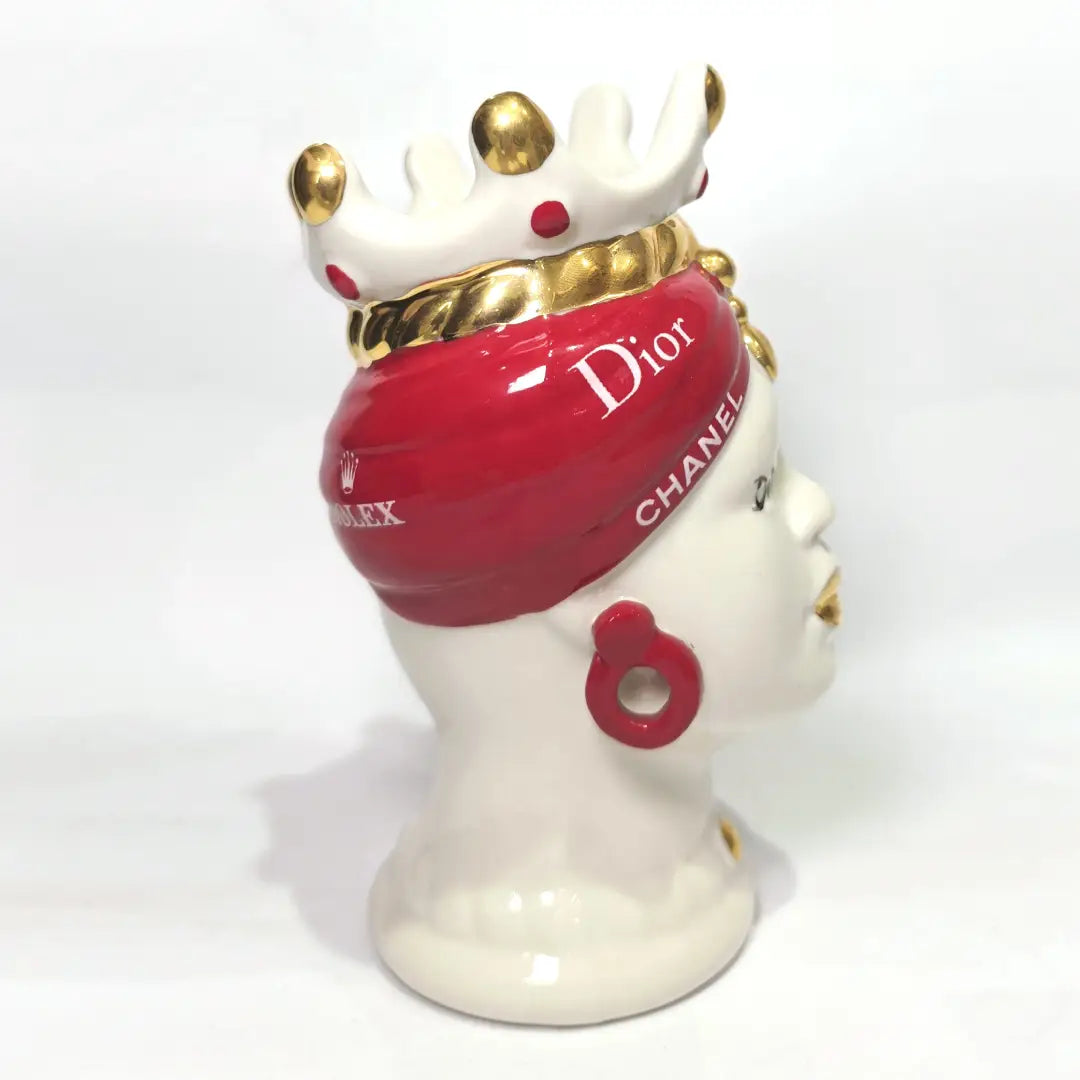 Coppia di Teste di Moro in ceramica bianca lucida con turbanti rosso ciliegia decorati da loghi fashion bianchi, completate da corone regali e labbra con finitura in oro zecchino. Queste sculture ornamentali di design pop art fondono la tradizione ceramica siciliana con l'estetica del lusso moderno, rappresentando un complemento d'arredo audace ed esclusivo per interni ricercati.
