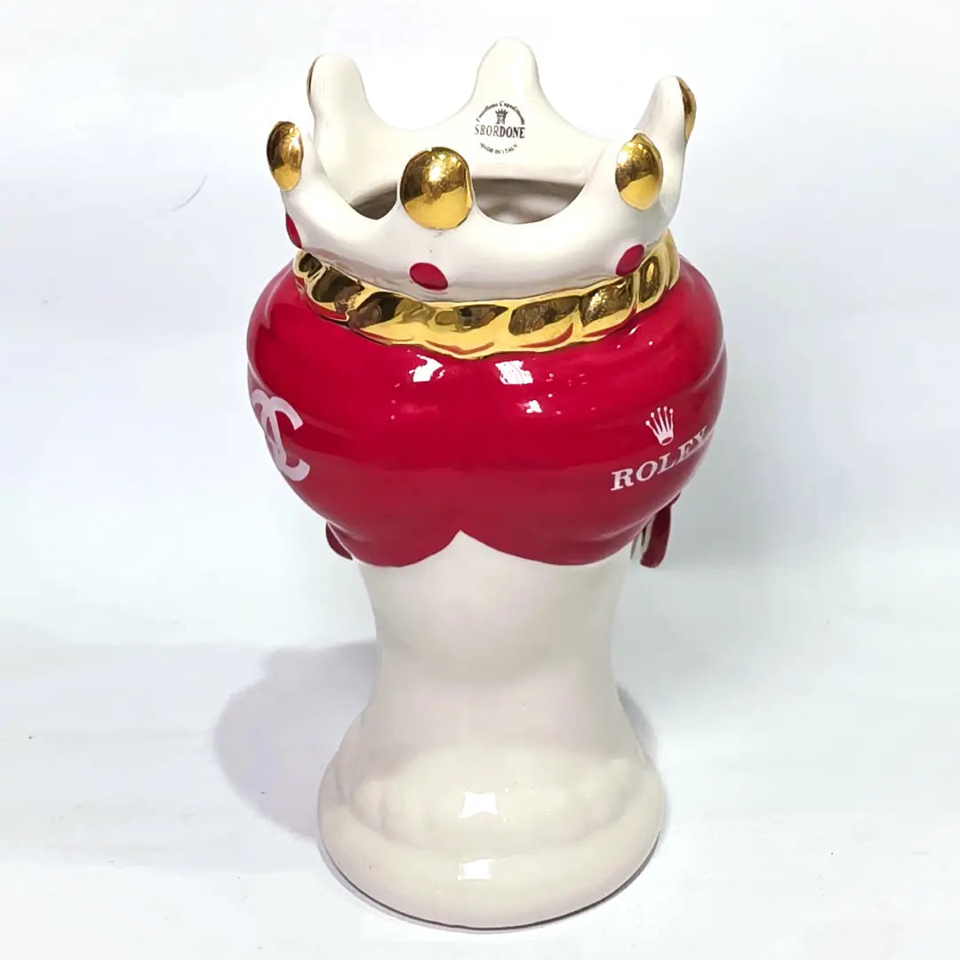 Coppia di Teste di Moro in ceramica bianca lucida con turbanti rosso ciliegia decorati da loghi fashion bianchi, completate da corone regali e labbra con finitura in oro zecchino. Queste sculture ornamentali di design pop art fondono la tradizione ceramica siciliana con l'estetica del lusso moderno, rappresentando un complemento d'arredo audace ed esclusivo per interni ricercati.