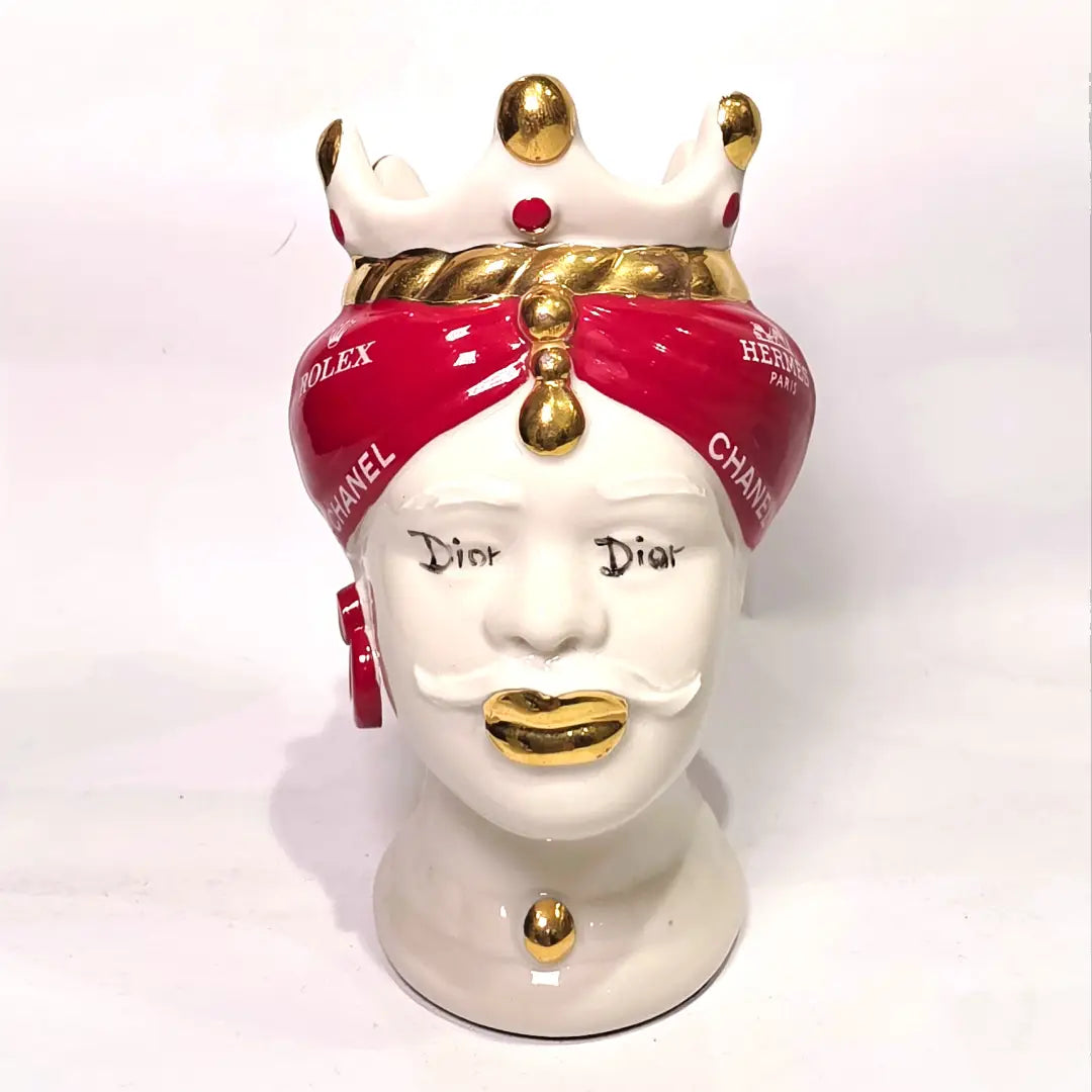 Coppia di Teste di Moro in ceramica bianca lucida con turbanti rosso ciliegia decorati da loghi fashion bianchi, completate da corone regali e labbra con finitura in oro zecchino. Queste sculture ornamentali di design pop art fondono la tradizione ceramica siciliana con l'estetica del lusso moderno, rappresentando un complemento d'arredo audace ed esclusivo per interni ricercati.