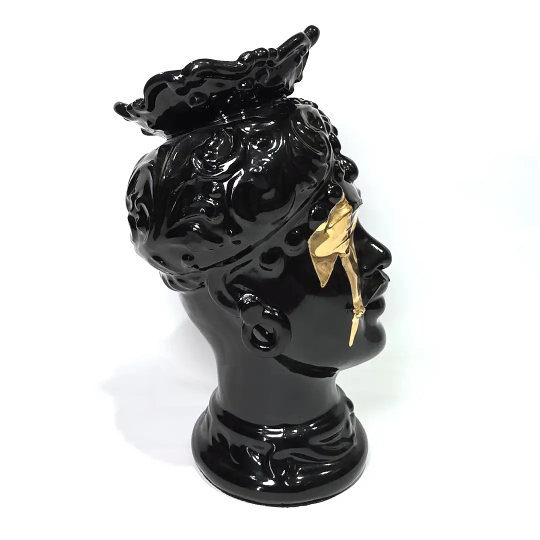 Coppia di Teste di Moro in ceramica artigianale, una in bianco lucido e una in nero lucido, entrambe caratterizzate da un'originale saetta dorata dipinta sul volto. Queste sculture ornamentali dal design pop e contemporaneo fondono la tradizione siciliana con uno stile d'avanguardia, rappresentando un complemento d'arredo iconico ed elegante per interni di lusso.