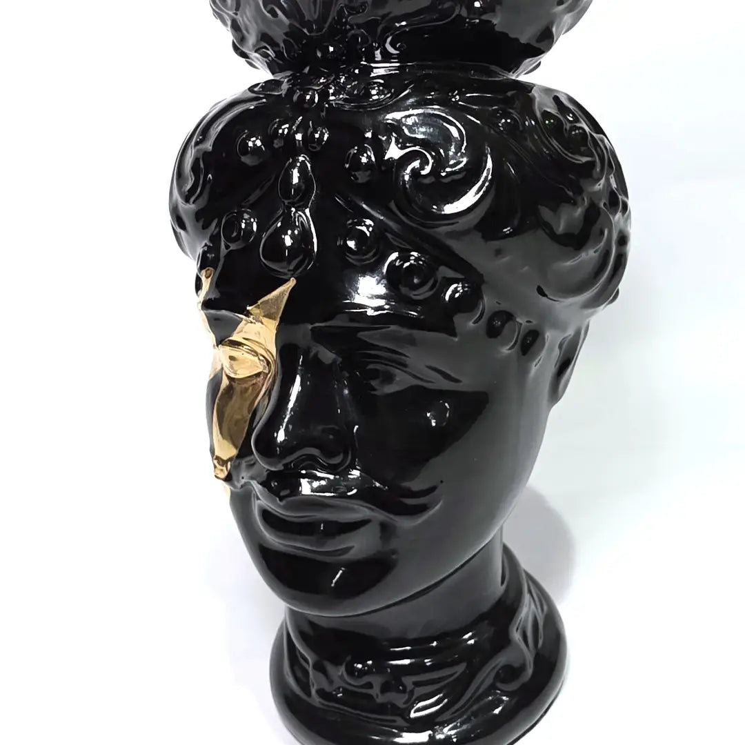 Coppia di Teste di Moro in ceramica artigianale, una in bianco lucido e una in nero lucido, entrambe caratterizzate da un'originale saetta dorata dipinta sul volto. Queste sculture ornamentali dal design pop e contemporaneo fondono la tradizione siciliana con uno stile d'avanguardia, rappresentando un complemento d'arredo iconico ed elegante per interni di lusso.