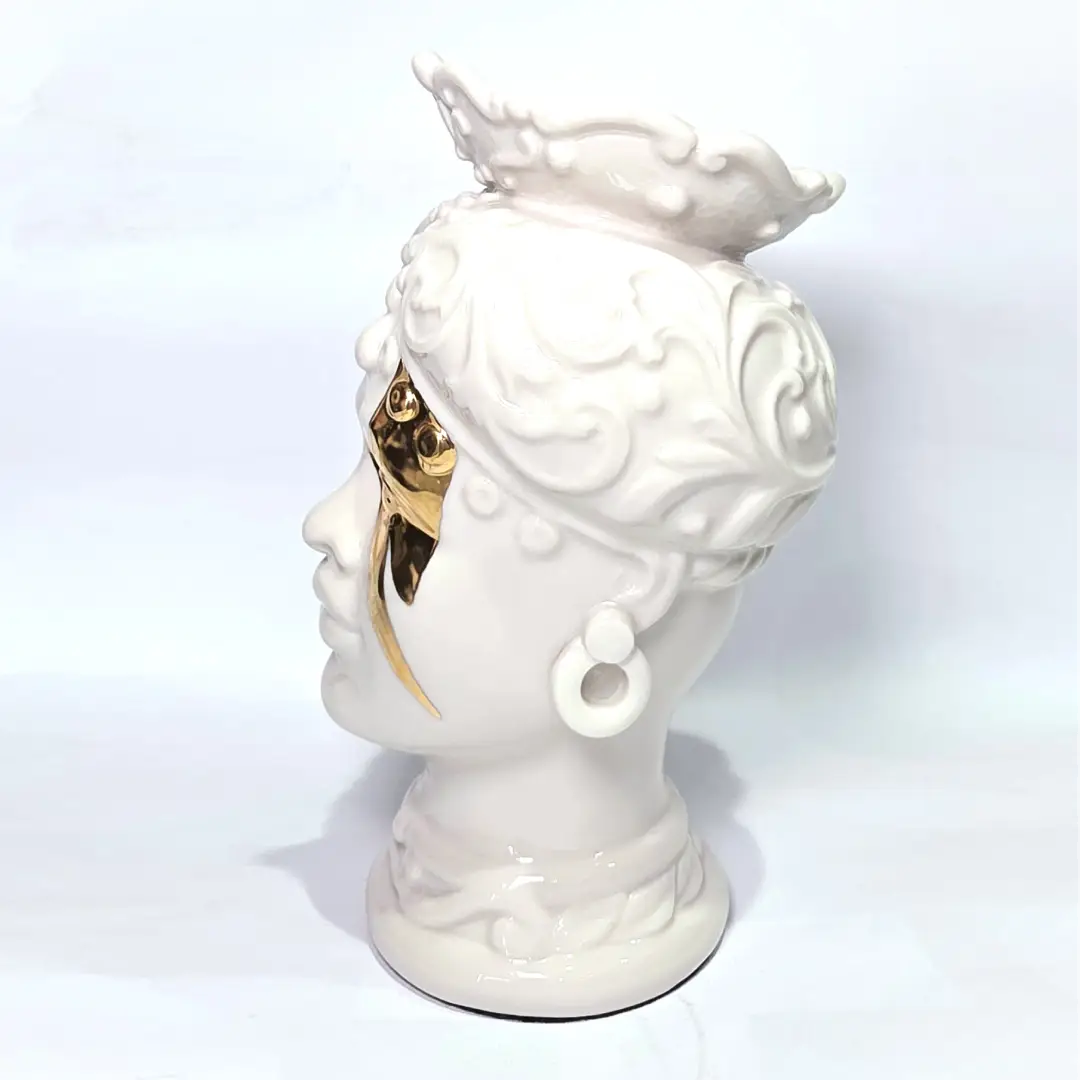 Coppia di Teste di Moro in ceramica artigianale, una in bianco lucido e una in nero lucido, entrambe caratterizzate da un'originale saetta dorata dipinta sul volto. Queste sculture ornamentali dal design pop e contemporaneo fondono la tradizione siciliana con uno stile d'avanguardia, rappresentando un complemento d'arredo iconico ed elegante per interni di lusso.