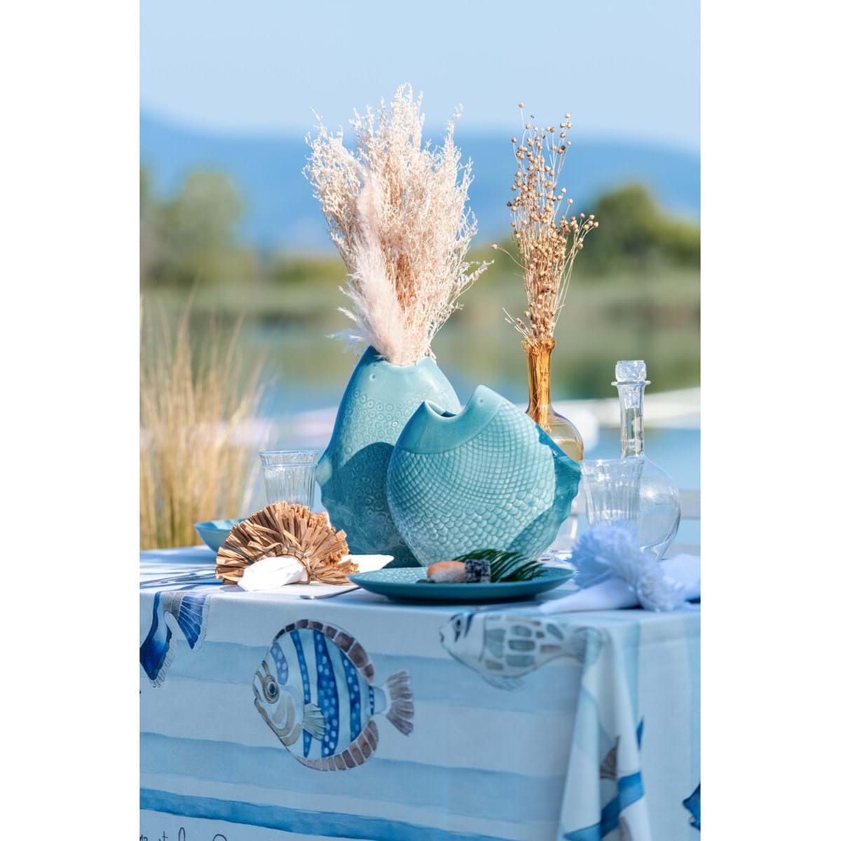 Dettaglio della tovaglia Blanc Mariclo' linea "La Mer et Les Poissons" in stile marinière. Stampa con pesci tropicali illustrati in azzurro e beige su fondo a righe orizzontali celesti. Bordo decorativo con scritte calligrafiche.