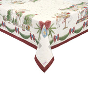 Dettaglio dell'angolo di una tovaglia natalizia in cotone Nuvole di Stoffa "La Giostra di Amelie". Il design presenta cavalli da giostra, ghirlande di pino e fiocchi rossi su un fondo panna stellato, rifinito da un bordo rosso scuro e l'etichetta del brand sull'orlo.