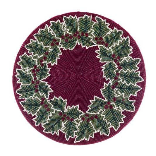Tovaglietta rotonda rossa Blanc Mariclò ricamata con perline. Presenta una ghirlanda circolare di foglie di agrifoglio verdi con venature bianche e bacche rosse su fondo bordeaux. Decoro natalizio.