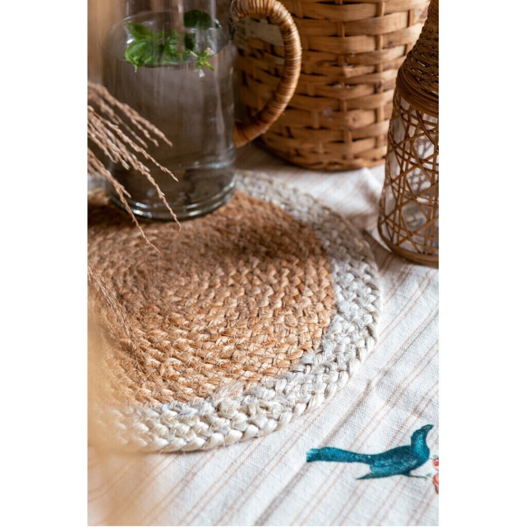 Tovaglietta americana tonda in juta intrecciata a mano, con centro naturale color paglia e bordo esterno bianco panna. Sottopiatto artigianale dallo stile country chic, ideale per apparecchiare la tavola con un tocco naturale ed elegante.