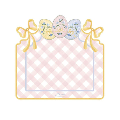 Tovaglietta americana in vinile della collezione "Pretty Easter" firmata Blanc Mariclo' con un motivo a scacchi bianchi e rosa perfetto per la colazione o il pranzo pasquale. La tovaglietta sagomata è decorata sul bordo superiore con fiocchi gialli e tre uova di Pasqua colorate nei toni pastello con dettagli floreali azzurri.