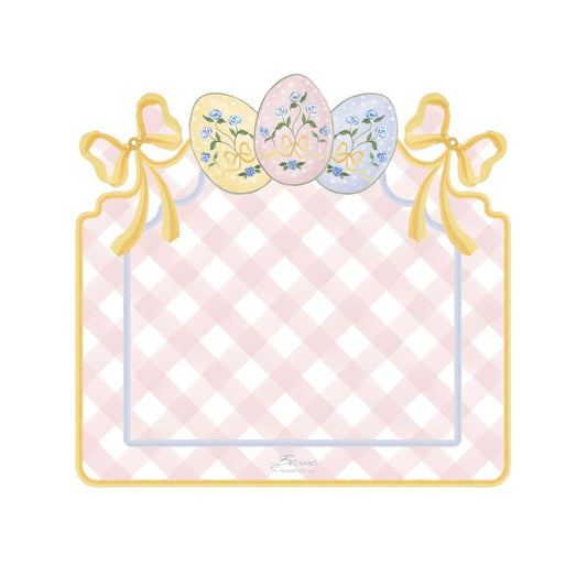 Tovaglietta americana in vinile della collezione "Pretty Easter" firmata Blanc Mariclo' con un motivo a scacchi bianchi e rosa perfetto per la colazione o il pranzo pasquale. La tovaglietta sagomata è decorata sul bordo superiore con fiocchi gialli e tre uova di Pasqua colorate nei toni pastello con dettagli floreali azzurri.