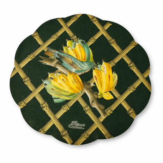 Tovaglietta tonda sagomata in vinile Blanc Mariclò collezione "Tropical". Su un fondo verde scuro, un'illustrazione centrale ritrae un uccellino esotico turchese tra caschi di banane gialle, sovrapposti a un motivo a graticcio di bambù dorato.