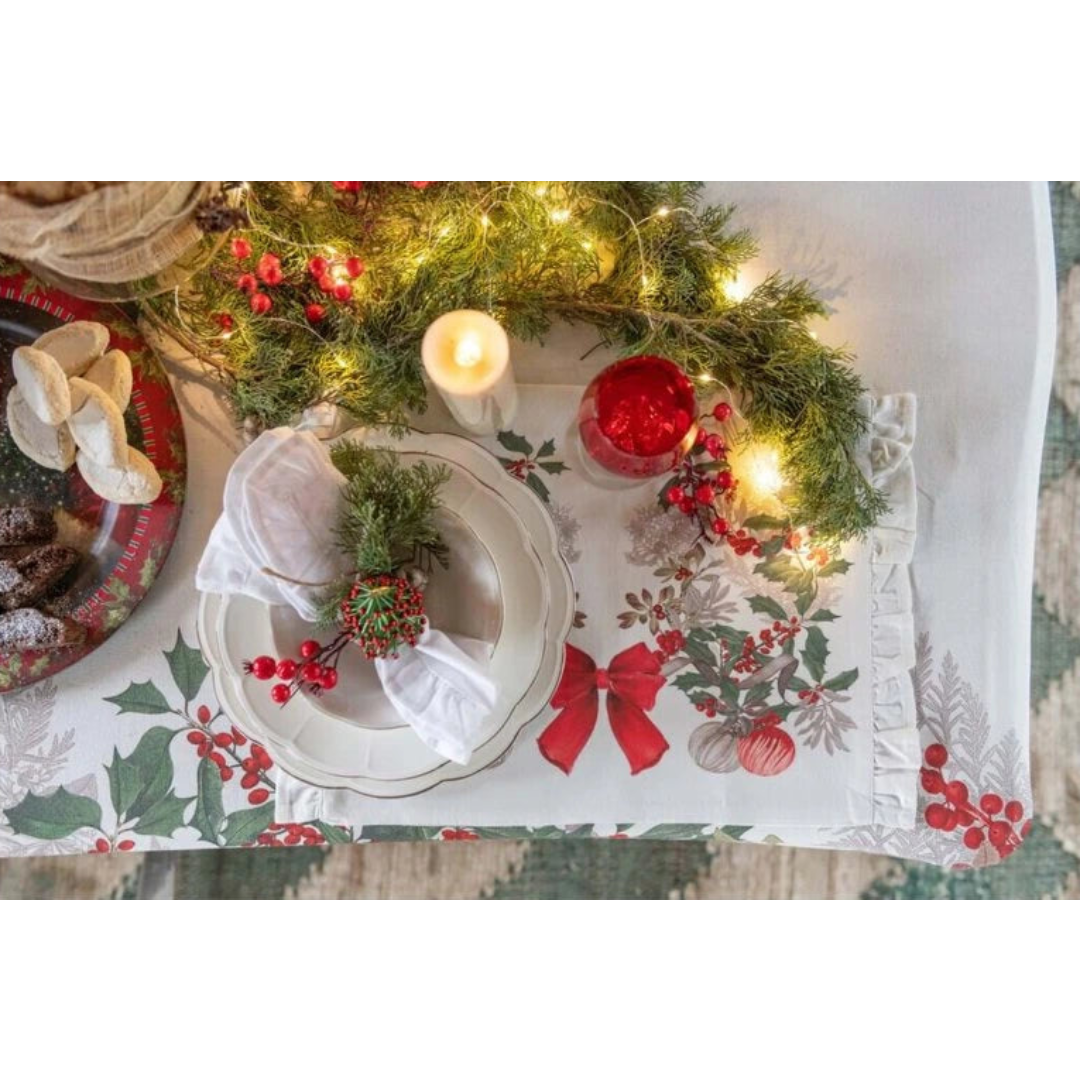 Tovaglietta americana natalizia Blanc Mariclò con stampa di ghirlande di agrifoglio, bacche rosse e palline di Natale appese a un grande fiocco scarlatto su fondo bianco. Stile festivo raffinato.