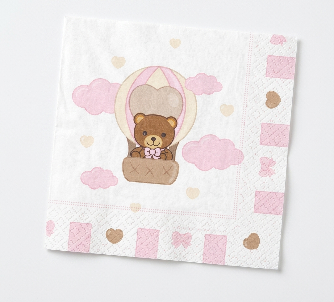 Tovagliolo di carta bianco con bordi decorati da cuori e fiocchi rosa; al centro un'illustrazione di un orsetto che vola in mongolfiera tra nuvole rosa e piccoli cuori pastello.