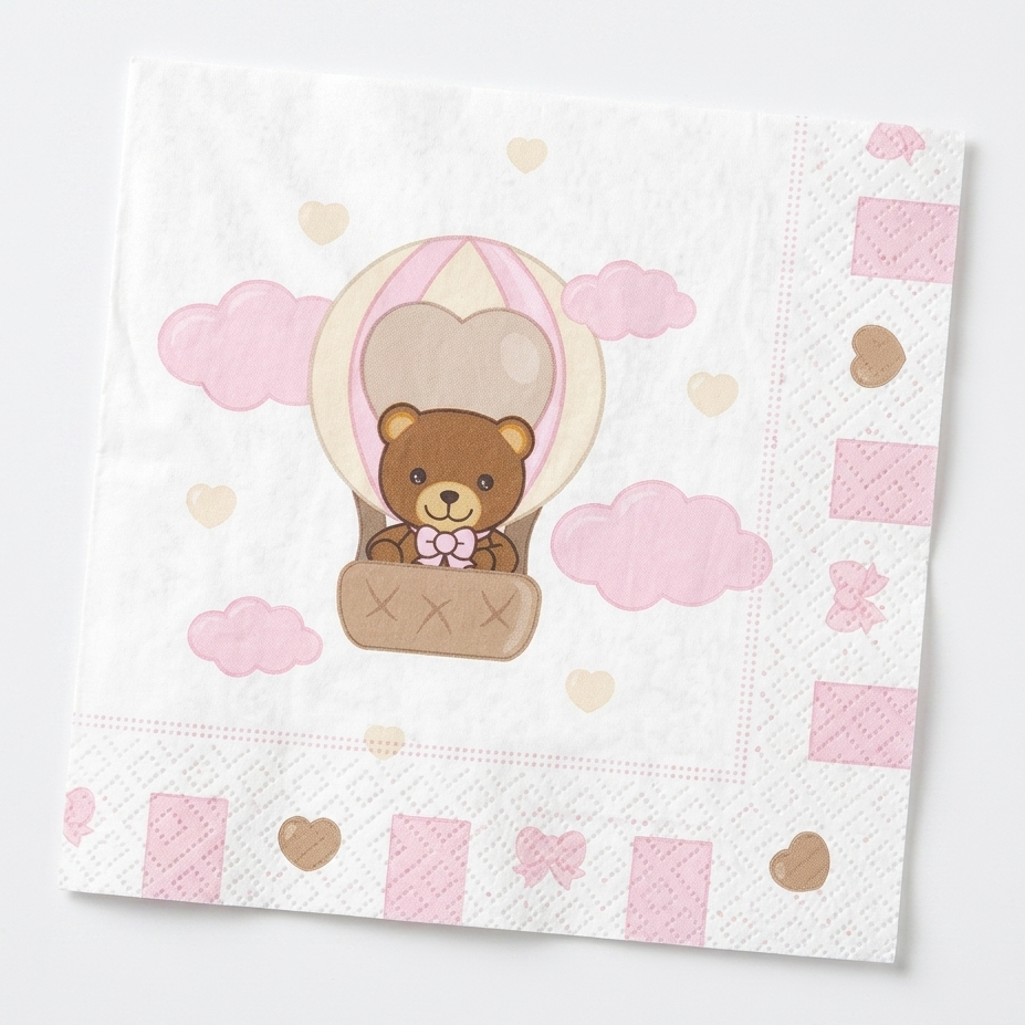 Tovagliolo di carta bianco con bordi decorati da cuori e fiocchi rosa; al centro un'illustrazione di un orsetto che vola in mongolfiera tra nuvole rosa e piccoli cuori pastello.