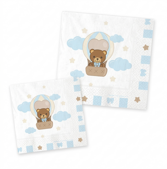 Tovagliolo di carta bianco con bordi decorati da stelline e fiocchi celeste; al centro un'illustrazione di un orsetto che vola in mongolfiera tra nuvole celeste e piccole stelle pastello.