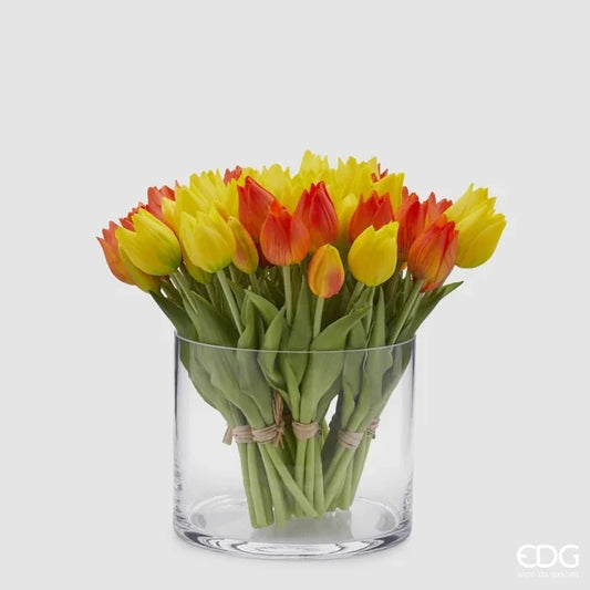 Un ricco bouquet di tulipani in silicone gialli e arancioni mescolati all'interno di un vaso di vetro cilindrico trasparente.