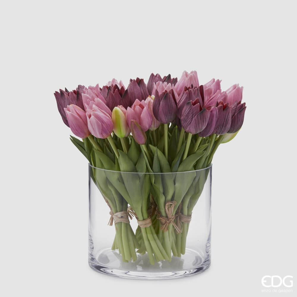 Un ricco bouquet di tulipani in silicone viola e malva mescolati all'interno di un vaso di vetro cilindrico trasparente.