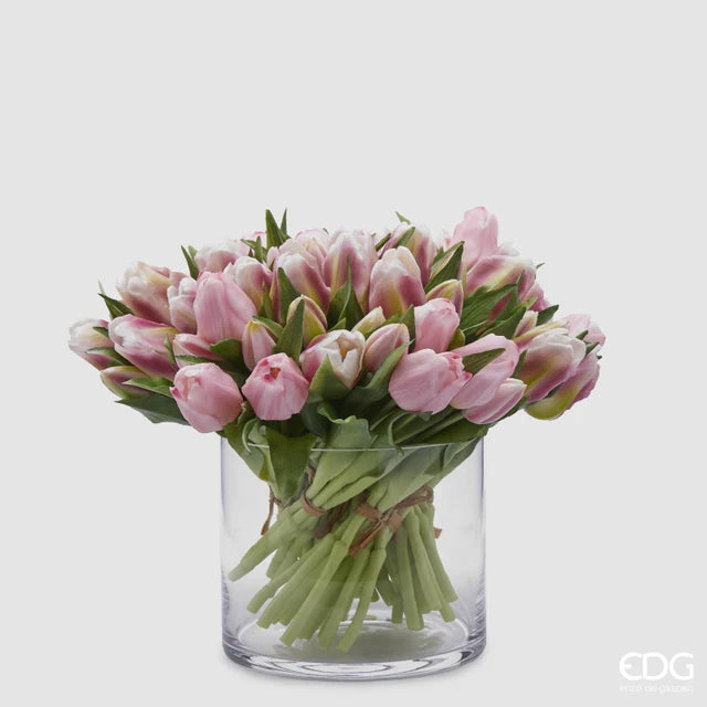Un ricco bouquet di tulipani in silicone malva e rosa mescolati all'interno di un vaso di vetro cilindrico trasparente.