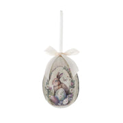Decorazione pasquale Blanc Mariclò a forma di uovo color crema con fiocco avorio. Il decoro mostra un coniglietto tra uova colorate e ghirlande di fiori campestri.