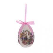 Decorazione pasquale a forma di uovo rosa pastello firmata Blanc Mariclò con nastro in raso coordinato. Il decoro centrale in stile vintage illustra due coniglietti bianchi all'interno di un cesto intrecciato, circondati da una ricca ghirlanda di fiori rosa e viola.